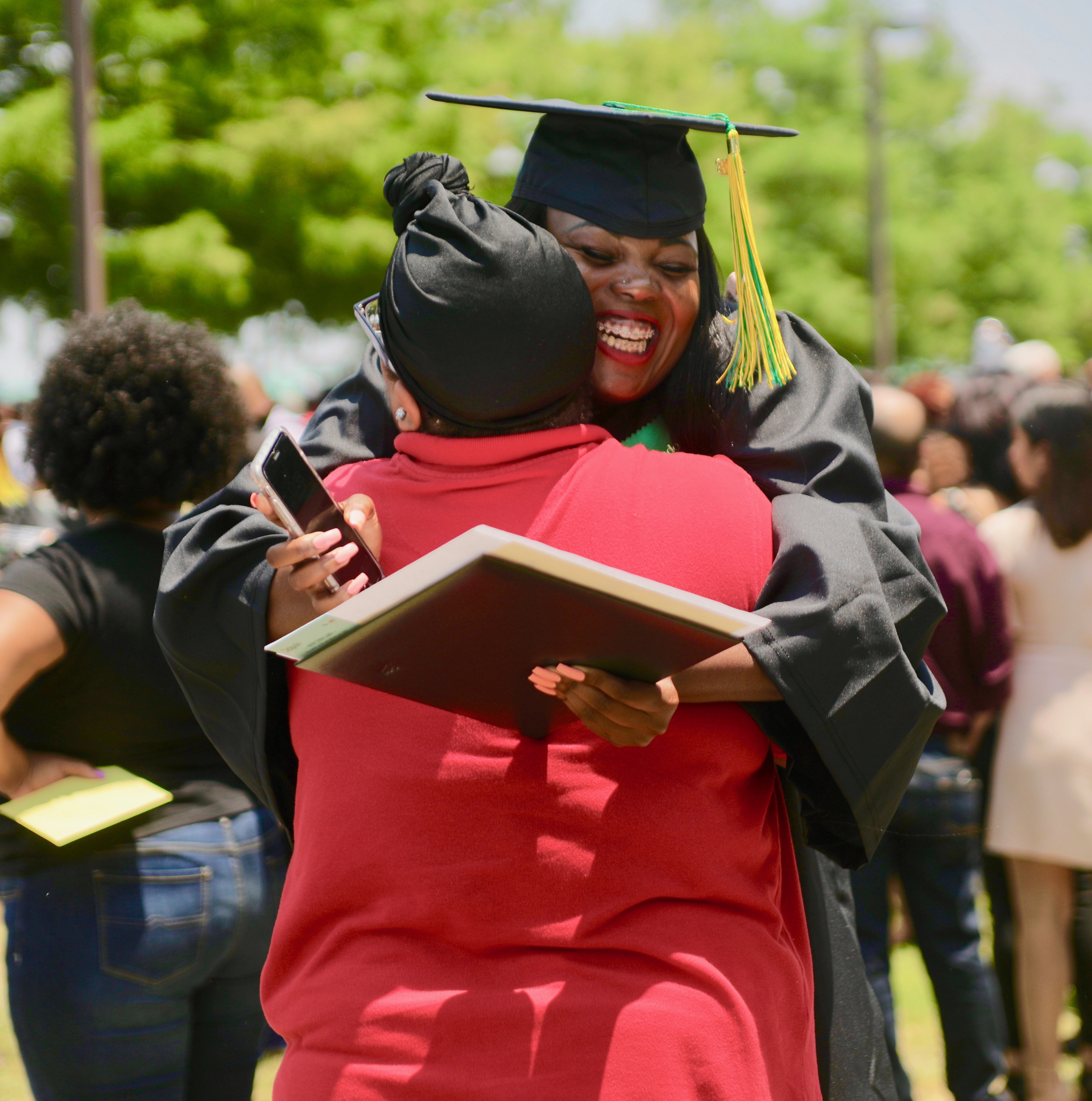 African-American female Delgado graduate smiling and hugging family member at commencement ceremony